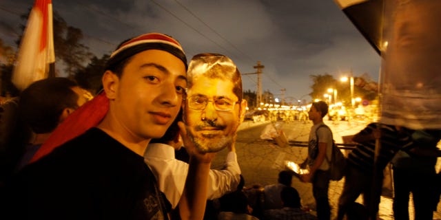 A supporter of Egypt's ousted President Mohammed Morsi poses with a paper mask of Morsi as he and others face the Egyptian military soldiers near the presidential palace in Cairo, Egypt, Saturday, July 13, 2013. Tens of thousands of Islamists rallied Friday in cities across Egypt, vowing to sustain for months their campaign to restore deposed President Mohammed Morsi to power. (AP Photo/Nasser Shiyoukhi)