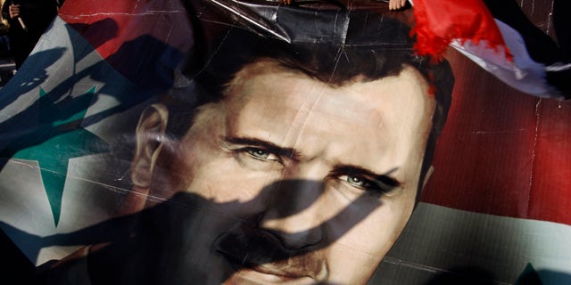 Dec. 16, 2011: Shadows of Syrians are reflected on a giant poster showing President Bashar Assad, during a supporting rally in Damascus, Syria.