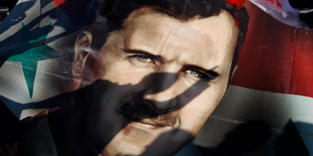 Dec. 16, 2011: Shadows of Syrians are reflected on a giant poster showing President Bashar Assad, during a supporting rally in Damascus, Syria.