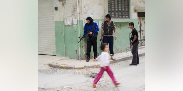 May 14, 2012: In this photo, a girl walks past Syrian rebels at Khaldiyeh neighborhood in Homs province, central Syria.