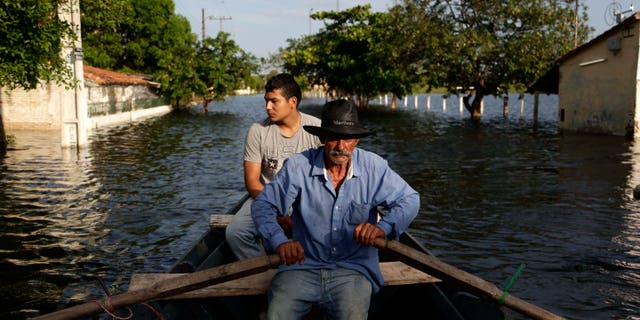 Victor Ferreira, who is displaced by flooding, rows his boat through the streets of his Jukyty neighborhood in Asuncion, Paraguay, Wednesday, Dec. 23, 2015. The Paraguay River is at its highest level since 1984 and threatening the poor districts that surround the capital, forcing about 100,000 people to shelters. (AP Photo/Jorge Saenz)