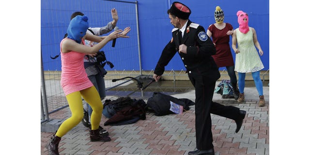 February 19, 2014: A Cossack militiaman attacks Nadezhda Tolokonnikova and a photographer as she and fellow members of the punk group Pussy Riot, including Maria Alekhina, right, in the pink balaclava, stage a protest performance in Sochi, Russia. The group had gathered in a downtown Sochi restaurant, about 21miles from where the Winter Olympics are being held. They ran out of the restaurant wearing brightly colored clothes and ski masks and were set upon by about a dozen Cossacks, who are used by police authorities in Russia to patrol the streets. (AP Photo/Morry Gash)