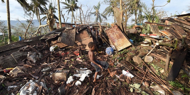 March 16, 2015: Samuel, only his first name given, kicks a ball through the ruins of their family home as his father, Phillip, at back, picks through the debris in Port Vila, Vanuatu in the aftermath of Cyclone Pam. (AP)