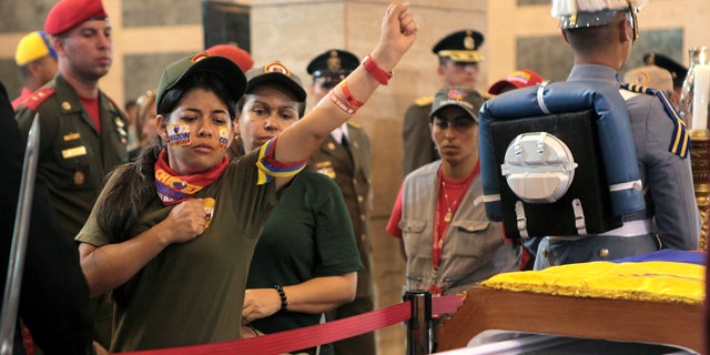 March 7, 2013: In this photo released by Miraflores Press Office, a woman pays her respects, placing a hand on her heart and saluting,  before she files past the glass-topped casket containing the remains of Venezuela's late President Hugo Chavez at the military academy, where he started his army career, in Caracas.