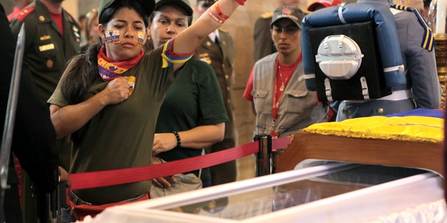 March 7, 2013: In this photo released by Miraflores Press Office, a woman pays her respects, placing a hand on her heart and saluting, before she files past the glass-topped casket containing the remains of Venezuela's late President Hugo Chavez at the military academy, where he started his army career, in Caracas.