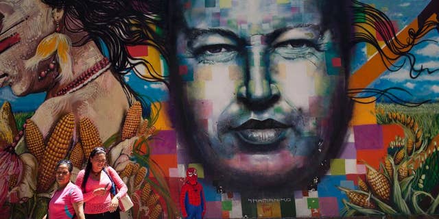 A boy dressed in a Spiderman costume poses for a photo next to a mural of Venezuela's late President Hugo Chavez painted on a wall of the Museo de Bellas Artes in Caracas, Venezuela, Tuesday, March 4, 2014. He’s been dead a year, but Chavez’s face and voice are everywhere. He bangs out the national anthem on state radio every morning and the national guard has even blasted his voice reciting poetry to drive rock-throwing protesters off the street. (AP Photo/Rodrigo Abd)