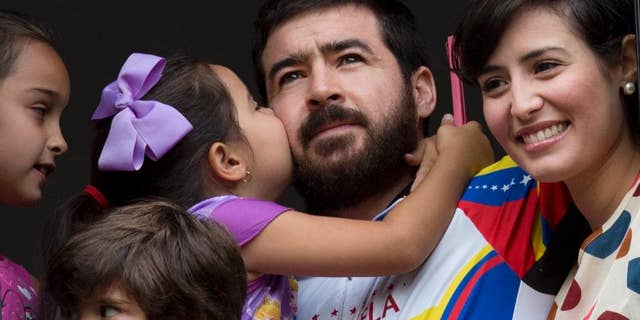 Maria Daniela kisses her father Daniel Ceballos, former mayor of the western city of San Cristobal, as he looks out from an apartment window with his wife Patricia de Ceballos, right, daughter Maria Veronica, left, and son Juan Daniel in Caracas, Venezuela, Wednesday, Aug. 12, 2015. One of Venezuela's most prominent opposition leaders started his first day of house arrest Wednesday after a surprise release following a year and a half in prison. The 31-year-old leader, who is awaiting trial on charges of civil rebellion, suffered from kidney and stomach problems during a 20-day hunger strike in June, according to his supporters. (AP Photo/Ariana Cubillos)