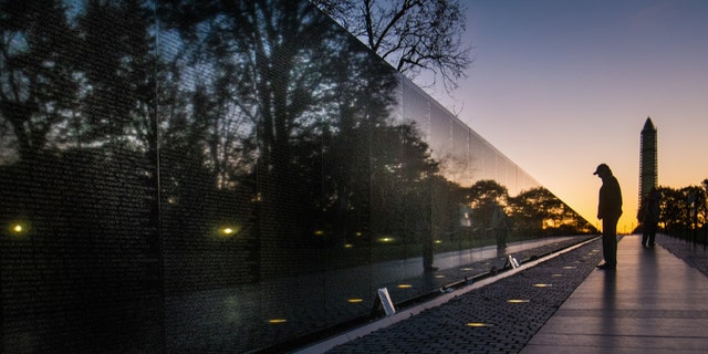 A visitor at the Vietnam War Memorial in Washington passes early in the morning on Veterans Day, Monday, Nov. 11, 2013, to look at the names inscribed on the wall. Several ceremonies are scheduled in the Nation's Capitol to honor those who have served in the U.S. military including a wreath laying at Vietnam War Memorial. The Washington Monument is at right. (AP Photo/J. David Ake)