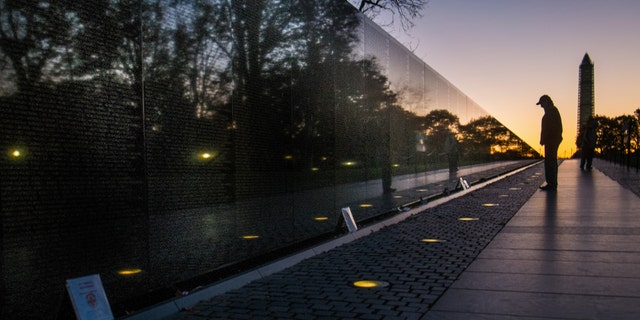 A visitor at the Vietnam War Memorial in Washington passes early in the morning on Veterans Day, Monday, Nov. 11, 2013, to look at the names inscribed on the wall. Several ceremonies are scheduled in the Nation's Capitol to honor those who have served in the U.S. military including a wreath laying at Vietnam War Memorial. The Washington Monument is at right. (AP Photo/J. David Ake)