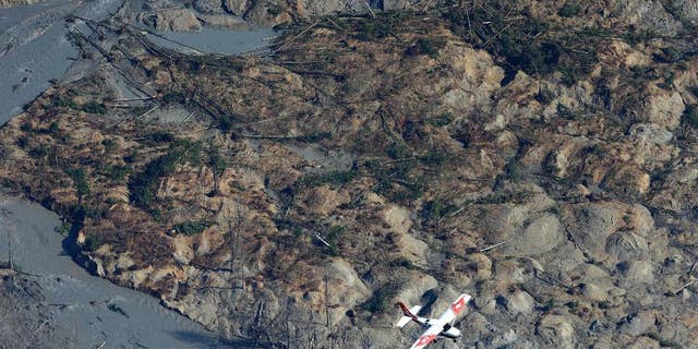 A Civil Air Patrol plane flies over the massive mudslide that killed at least eight people and left dozens missing as shown in this aerial photo, Monday, March 24, 2014, near Arlington, Wash. The search for survivors grew Monday raising fears that the death toll could climb far beyond the eight confirmed fatalities. (AP Photo/Ted S. Warren)