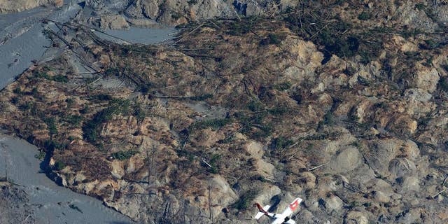 A Civil Air Patrol plane flies over the massive mudslide that killed at least eight people and left dozens missing as shown in this aerial photo, Monday, March 24, 2014, near Arlington, Wash. The search for survivors grew Monday raising fears that the death toll could climb far beyond the eight confirmed fatalities. (AP Photo/Ted S. Warren)