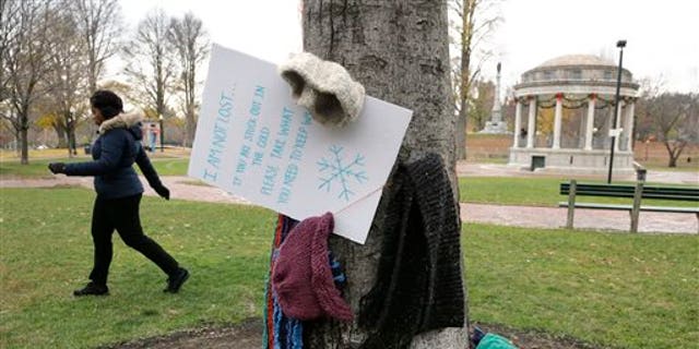 Hats and scarves hang on a tree near a sign that invites people in need to take them to keep warm, on the Boston Common Tuesday, Dec. 8, 2015, in Boston. A Good Samaritan has been hanging the cold weather items, as well as coats, gloves, and mittens, for the needy on trees in the park, a gesture that's warming the hearts of passersby. (AP Photo/Steven Senne)