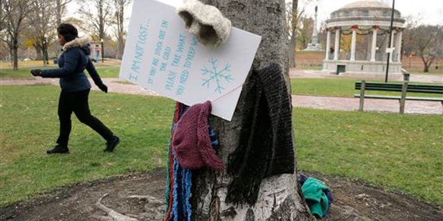 Hats and scarves hang on a tree near a sign that invites people in need to take them to keep warm, on the Boston Common Tuesday, Dec. 8, 2015, in Boston. A Good Samaritan has been hanging the cold weather items, as well as coats, gloves, and mittens, for the needy on trees in the park, a gesture that's warming the hearts of passersby. (AP Photo/Steven Senne)