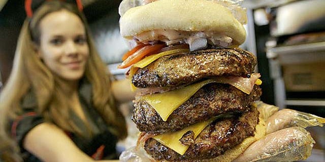 Courtney Chapman, a waitress dressed as a nurse at the Heart Attack Grill, holds up a triple bypass burger Friday, Dec. 1, 2006 in Tempe, Ariz.