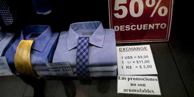 In this June 5, 2013 photo, a shop window displays a sign that reads in Spanish "50% discount" as well as the store's accepted rates of exchange in the informal market for the Argentine peso with the US dollar, the euro, and Brazil's real, along Florida street in Buenos Aires, Argentina. The weakening peso has led to a flood of day-trippers from neighboring countries into Argentina, which imposed severe currency controls in hopes of reducing the flight of dollars and protecting foreign reserves. (AP Photo/Natacha Pisarenko)