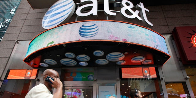 A man uses a cell phone as he walks past an AT&T store in New York.
