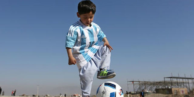 Murtaza Ahmadi, a five-year-old Afghan Lionel Messi fan plays with a soccer ball during a photo opportunity as he wears a shirt signed by Messi, in Kabul, Afghanistan, Friday, Feb. 26, 2016.  Mohammad Arif Ahmadi, the father of the boy who was pictured wearing a homemade Argentina shirt with No. 10 on the back, said Friday they want to thank Messi, a UNICEF goodwill ambassador, in person.(AP Photo/Rahmat Gul)