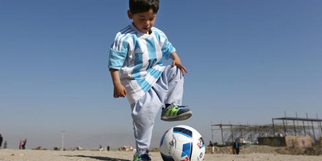 Murtaza Ahmadi, a five-year-old Afghan Lionel Messi fan plays with a soccer ball during a photo opportunity as he wears a shirt signed by Messi, in Kabul, Afghanistan, Friday, Feb. 26, 2016. Mohammad Arif Ahmadi, the father of the boy who was pictured wearing a homemade Argentina shirt with No. 10 on the back, said Friday they want to thank Messi, a UNICEF goodwill ambassador, in person.(AP Photo/Rahmat Gul)