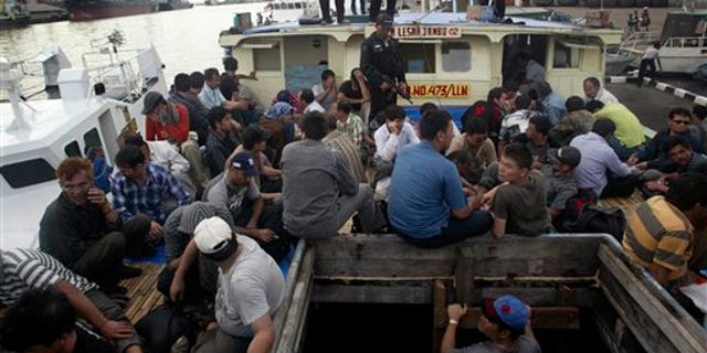 May 2, 2010: Indonesian marine police officers watch as Afghan asylum seekers sit on their ship that was caught off Java island upon docking at Tanjung Perak port in Surabaya, East Java, Indonesia.