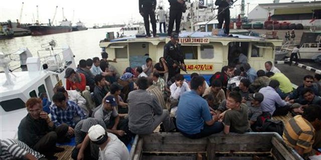 May 2, 2010: Indonesian marine police officers watch as Afghan asylum seekers sit on their ship that was caught off Java island upon docking at Tanjung Perak port in Surabaya, East Java, Indonesia.