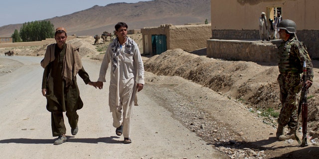 May 17, 2012, Two men walk hand-in-hand past an Afghan National Army soldier in east Afghanistan.