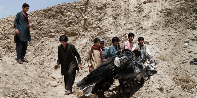Aug. 12, 2012: Afghans push parts of a damaged vehicle off a hill after a roadside explosion on the outskirts of Laghman province east of Kabul, Afghanistan.
