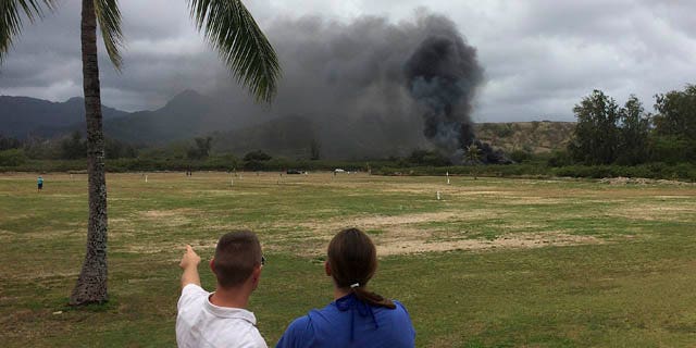 May 17, 2015: A man and woman look toward smoke rising from a Marine Corps Osprey aircraft after making a hard landing on Bellows Air Force Station near Waimanalo, Hawaii. The fatal crash of the Marine Corps' new hybridized airplane-and-helicopter aircraft during a training exercise is renewing safety concerns about the machine. (Zane Dulin via AP)