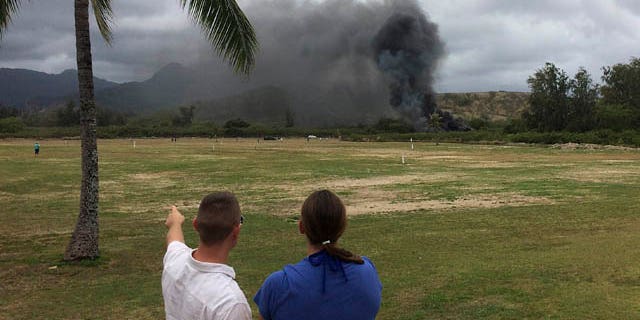 May 17, 2015: A man and woman look toward smoke rising from a Marine Corps Osprey aircraft after making a hard landing on Bellows Air Force Station near Waimanalo, Hawaii. The fatal crash of the Marine Corps' new hybridized airplane-and-helicopter aircraft during a training exercise is renewing safety concerns about the machine. (Zane Dulin via AP)