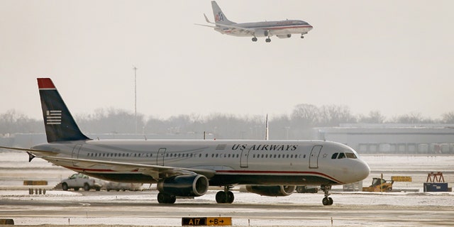 CHICAGO, IL - DECEMBER 09: An American Airlines jet flies over a US Airways jet at O'Hare Airport on December 9, 2013 in Chicago, Illinois. American Airlines announced today that it had completed a merger deal with US Airways. The deal will make American Airlines the world's largest airline, flying about 6,700 flights per day. (Photo by Scott Olson/Getty Images)
