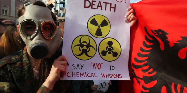 Nov. 14, 2013 - An Albanian student wears a gas mask and holds a sign during a protest against the dismantling of Syrian chemical weapons in Albania at the Prime Minister's office in Tirana.