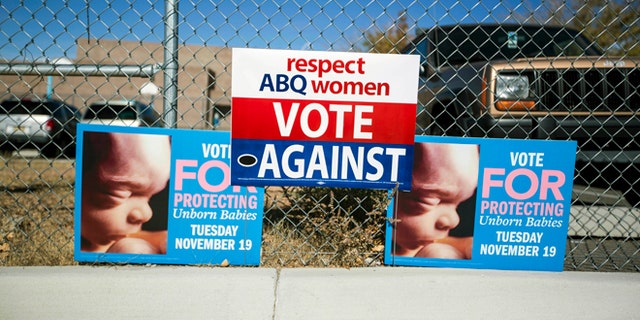 Signs advocating for and against a late term abortion ban hang on a fence outside of a voting site at Eisenhower Middle School in Albuquerque, N.M., Tuesday, Nov. 19, 2013. Albuquerque voters will decide whether to ban abortions after 20 weeks following an emotional and graphic campaign that has included protests and hundreds of thousands of dollars on television and radio ads that have brought out more than twice as many early voters as the recent mayoral elections. (AP Photo/Juan Antonio Labreche)