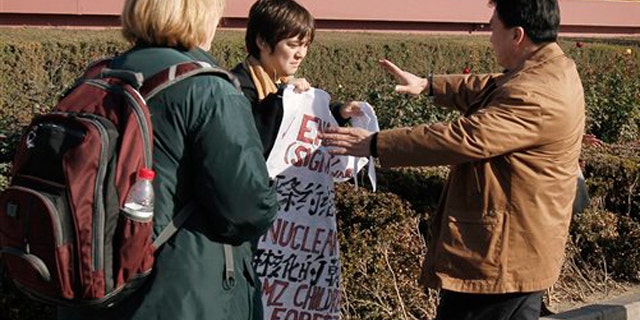 A plain clothes policeman, right, rushes to stop Jonathan Lee, center, after he unfurled a banner sign saying "peace treaty" and "nuclear free DMZ children's peace forest" outside the Forbidden City in Beijing Monday, Nov. 22, 2010. Lee, 13, of Ridgeland, Miss., campaigning to turn the demilitarized zone between North and South Korea into a peace park was taken away by Chinese police after staging a brief protest near Tiananmen Square.