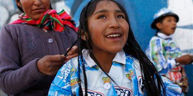 An indigenous woman braids her daughter's hair before the start of a parade in El Alto, Bolivia, Friday, Oct. 23, 2015.