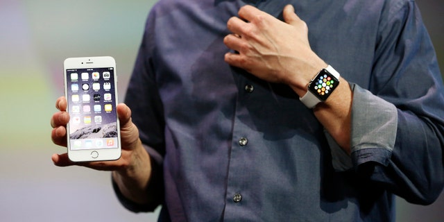Apple CEO Tim Cook wears the Apple Watch and shows the iPhone 6 Plus during an Apple event at the Flint Center in Cupertino, California.