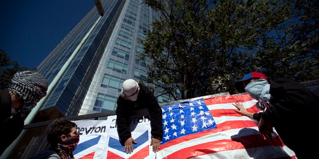 Demonstrators place a U.S. flag and a Chevron sign on a fence in front of Argentina's state-controlled YPF oil company headquarters to protest a deal between YPF and U.S. oil company Chevron in Buenos Aires, Argentina, Tuesday, July 16, 2013. YPF, which was expropriated in 2012 from Spain's Repsol, is finalizing the details of an agreement with Chevron which would invest in the first pilot for massive exploration for unconventional oil and gas in the Vaca Muerta region. (AP Photo/Victor R. Caivano)