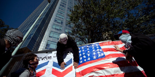 Demonstrators place a U.S. flag and a Chevron sign on a fence in front of Argentina's state-controlled YPF oil company headquarters to protest a deal between YPF and U.S. oil company Chevron in Buenos Aires, Argentina, Tuesday, July 16, 2013. YPF, which was expropriated in 2012 from Spain's Repsol, is finalizing the details of an agreement with Chevron which would invest in the first pilot for massive exploration for unconventional oil and gas in the Vaca Muerta region. (AP Photo/Victor R. Caivano)