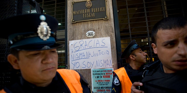 Policemen stand guard next to a sign that reads in Spanish; "Thanks Nisman. Justice. I am Nisman," outside the prosecutor's office investigating the death of Alberto Nisman, a prosecutor found dead in his apartment, in Buenos Aires, Argentina, Thursday, Jan. 22, 2015. The death of the prosecutor who had accused Argentinas President Cristina Fernandez of a criminal conspiracy came under mounting questions Wednesday with the discovery that the apartment where he was found dead had not been securely locked and had a third entrance. (AP Photo/Rodrigo Abd)