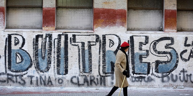 A woman walks by a graffiti that reads in Spanish "Vultures" in Buenos Aires, Argentina.