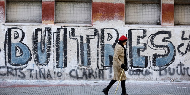 A woman walks by a graffiti that reads in Spanish "Vultures" in Buenos Aires, Argentina.