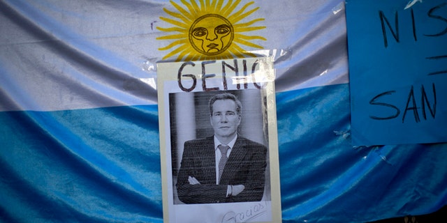 A portrait of late prosecutor Alberto Nisman is seen pasted on an Argentine flag with a title that reads in Spanish "Genius," outside a funeral home during his wake in Buenos Aires, Argentina, Thursday, Jan. 29, 2015. Nisman was scheduled to appear before congress the day after he was found dead in his apartment on Jan. 18, to detail his allegations that President Cristina Fernandez had conspired to protect some of the Iranian suspects in the 1994 bombing of a Jewish center. The man who gave Nisman the gun that killed him said Wednesday that Nisman feared for the safety of his daughters and didn't trust the policemen protecting him. (AP Photo/Rodrigo Abd)