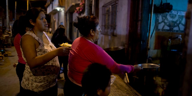 In this Oct. 13, 2016, women line up for a free dinner to take home to their families, from Norma Colque's soup kitchen in the Villa 31 neighborhood of Buenos Aires, Argentina. With the economy expected to shrink by 1.5 percent this year, President Mauricio Macri now admits his poverty goal isn't possible, and discontent is growing. (AP Photo/Natacha Pisarenko)