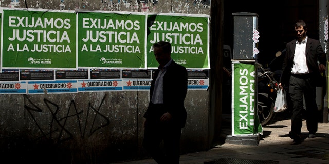 Men walk pass posters that read in Spanish "Demand justice to justice", in reference to march organized by federal prosecutors demanding justice after the death of special prosecutor Alberto Nisman almost a month ago, in Buenos Aires, Argentina, Friday, Feb. 13, 2015. Nisman accused President Cristina Fernandez, Foreign Minister Hector Timerman and others in her administration of brokering the cover-up in the bombing of a Jewish community center in exchange for favorable deals on oil and other goods from Iran. Fernandez and Timerman have strongly denied the accusations, and Iran has repeatedly denied involvement in the bombing, which killed 85 people. (AP Photo/Rodrigo Abd)