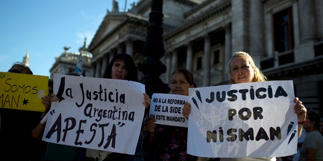 Women holds sign that reads in Spanish; "Argentine justice stinks," second left, "and "Justice for Nisman," right, during a march for justice and against impunity in the case of the mysterious death of late prosecutor Alberto Nisman, in Buenos Aires, Argentina, Wednesday, Feb. 4, 2015. Investigators examining the death of Nisman, who accused Argentine President Cristina Fernandez of agreeing to shield the alleged masterminds of a 1994 terror bombing, said Tuesday, they have found a draft document he wrote requesting her arrest. (AP Photo/Rodrigo Abd)