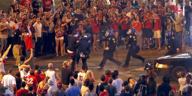 Tucson Police Officers rush out of their line to take a man into custody who had been taunting them and riling up a crowd of fans in Maingate Square, Saturday, March 29, 2014, in Tucson Ariz. following Arizona's loss to Wisconsin 64-63 in the West Region NCAA final. (AP Photo/Arizona Daily Star, Kelly Presnell)