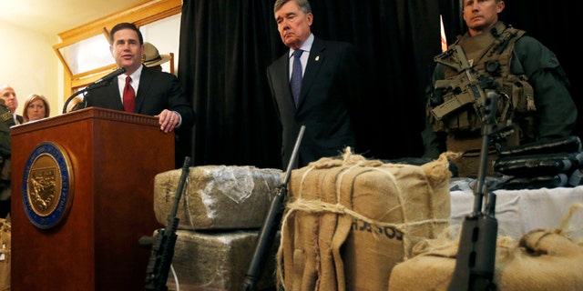 With seized drugs and weapons from border-crossing drug smugglers, Arizona Gov. Doug Ducey, left, speaks at a news conference after testifying at a field hearing of the U.S. Senate Homeland Security and Governmental Affairs Committee at the Arizona Capitol Monday, Nov. 23, 2015, in Phoenix.  R. Gil Kerlikowske, center, commissioner of the U.S. Customs and Border Protection, listens in during the news conference. (AP Photo/Ross D. Franklin)