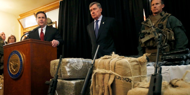 With seized drugs and weapons from border-crossing drug smugglers, Arizona Gov. Doug Ducey, left, speaks at a news conference after testifying at a field hearing of the U.S. Senate Homeland Security and Governmental Affairs Committee at the Arizona Capitol Monday, Nov. 23, 2015, in Phoenix. R. Gil Kerlikowske, center, commissioner of the U.S. Customs and Border Protection, listens in during the news conference. (AP Photo/Ross D. Franklin)