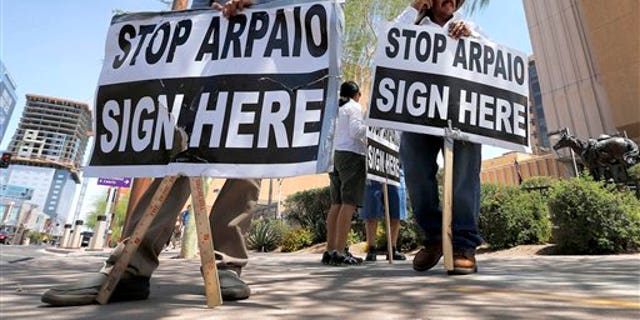 FILE - In this May 29, 2013, file photo, Simon Lopez, left, and Hiliaro Islas hold signs while trying to collect signatures in an effort to recall Maricopa County Sheriff Joe Arpaio, in downtown Phoenix. Arizona is still widely viewed in Mexico as the most anti-Mexico state in the U.S., even if the tough anti-migrant law behind that perception has been largely voided. But Arizonas leaders are logging lots of miles to put a new face on their home state. (AP Photo/Matt York, File)