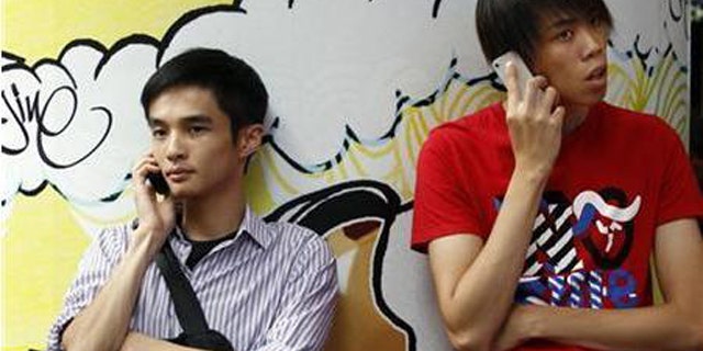 Aug. 16, 2011: Two men use mobile phones as they wait outside a department store in Hong Kong.