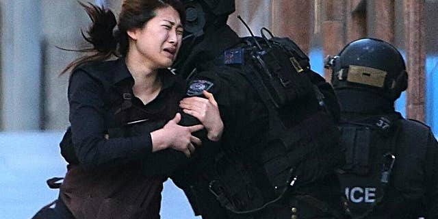 A hostage runs to armed tactical response police officers after escaping from a cafe under siege in Sydney, Australia. (AP Photo/Rob Griffith, File)