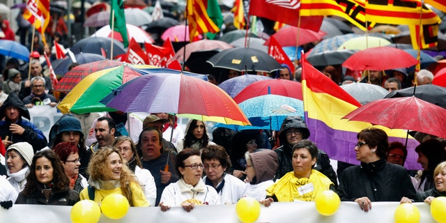 People hold umbrellas as they march with a banner during a protest against government austerity measures in Barcelona.